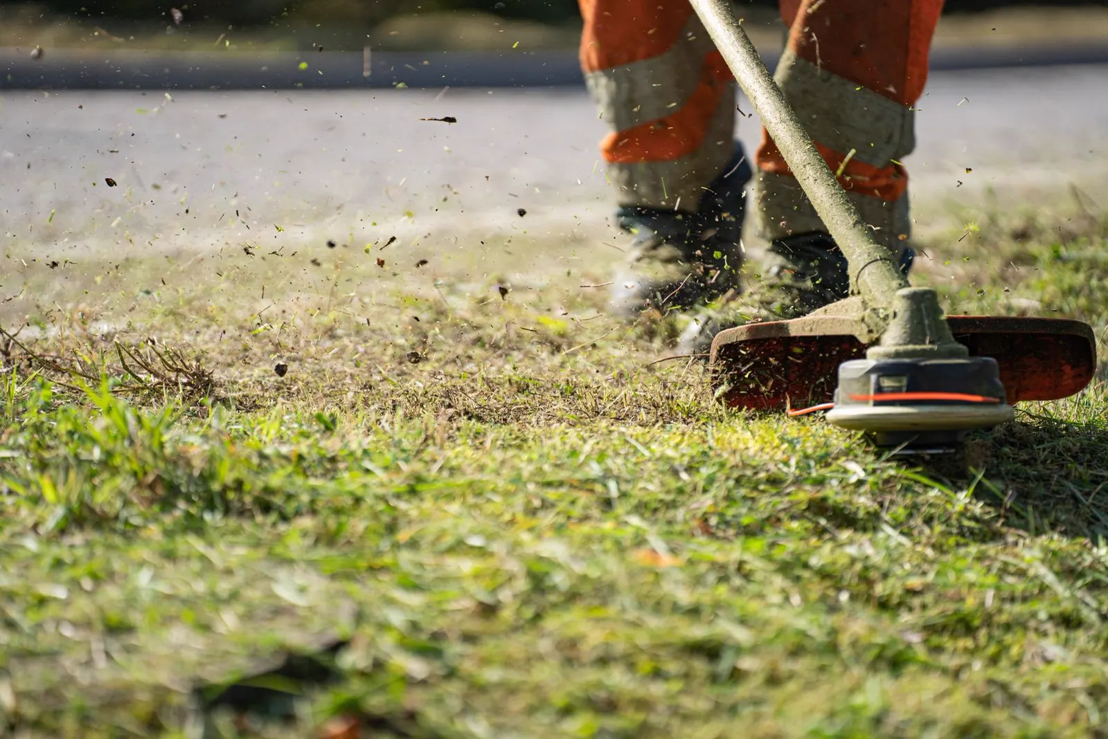 A worker trimming grass along an edge with a string trimmer