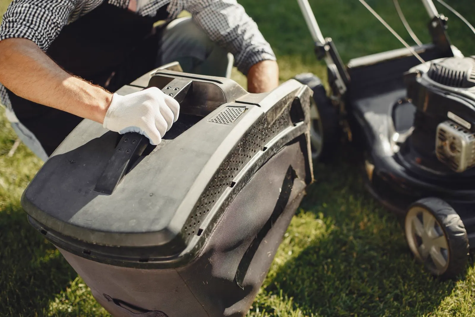 A lawn care worker emptying a mower's grass bag
