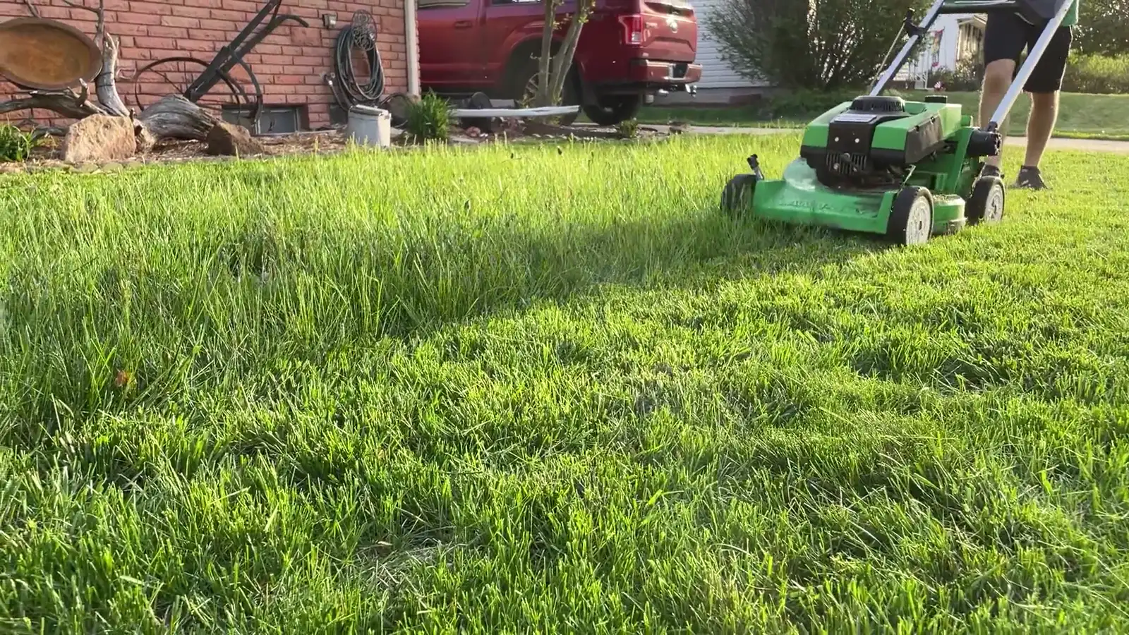 A push mower cutting a green front lawn in a residential neighborhood at golden hour